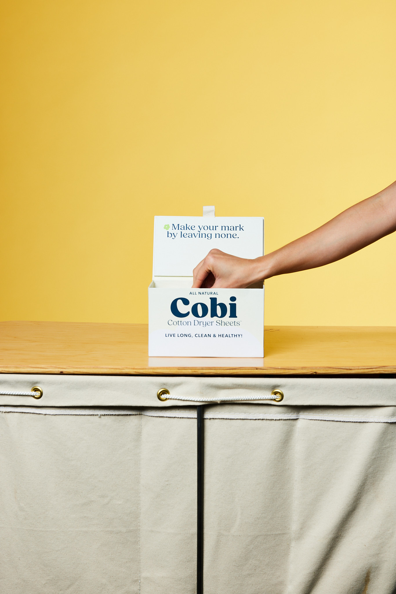 Hand pulling a Cobi Cotton Dryer Sheet from the open box
